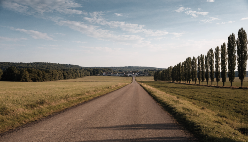 Route départementale rurale à l'approche d'un village, bas-côtés dégagés